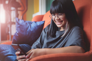 asian teenager reading message in smartphone with happiness face at home living room