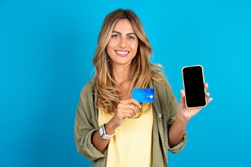 Photo of adorable young beautiful blonde woman wearing overshirt holding credit card and Smartphone. Reserved for online purchases