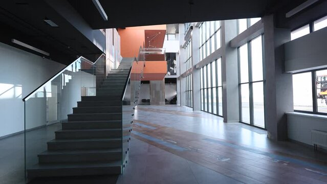 The camera pans across a spacious and empty hall inside a modern office building. The hall is filled with natural light coming through the large panoramic windows, creating an inviting atmosphere