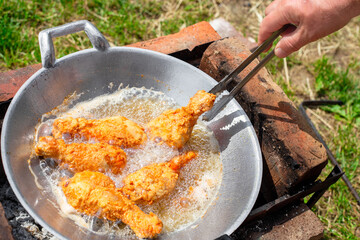 Fototapeta premium a man fries chicken drumsticks in batter in oil in a wok pan at the dacha. Cooking delicious food at a picnic.