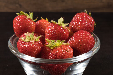 Strawberries in a glass bowl on a dark wooden background.