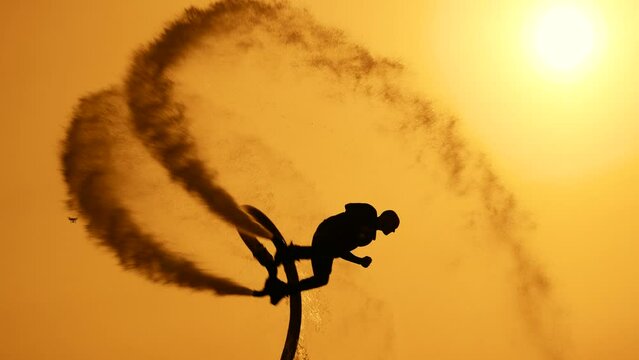 Epic scene at sunset. Silhouette of a flyboarder against the backdrop of the setting sun and sky. The athlete does somersaults in the air