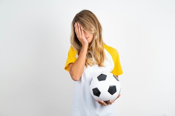 Young beautiful woman wearing football T-shirt over white background with sad expression covering...