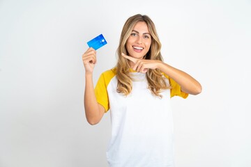 Smiling Young beautiful woman wearing football T-shirt over white background showing debit card pointing finger empty space