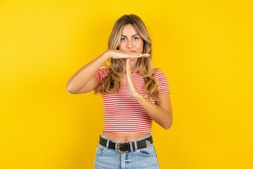 Young beautiful blonde woman wearing striped t-shirt over yellow studio background being upset...