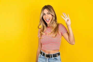 Young beautiful blonde woman wearing striped t-shirt over yellow studio background showing and...