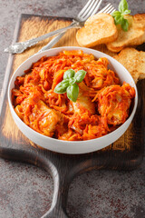 White fish fillet stewed with carrots, onions and celery in tomato sauce served with toast close-up on a wooden board on the table. Vertical