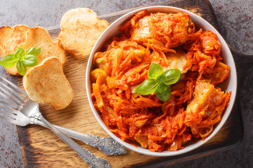 Delicious fish stew with vegetables in spicy tomato sauce served with toast close-up on a wooden board on the table. horizontal top view from above