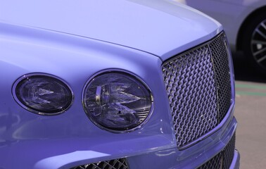 Unbranded SUV, sleek car closeup background image. Glistening newly cleaned car in the sunlight, blue paint scheme. Chrome grill and elegant headlights of car. Wallpaper of modern elegant luxury car.