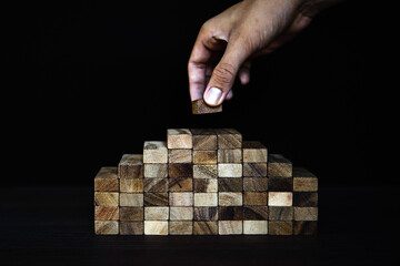 Hand placing wooden block tower stack in pyramid stair step with caution to prevent collapse or...