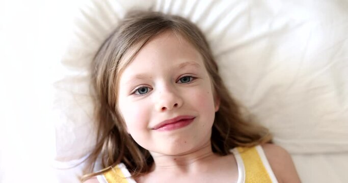 Funny little girl takes selfie and makes face and falls on bed. Smiling cute kid taking pictures and chatting