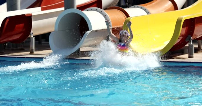 Happy girl child on water slide in water park. Children recreation in the children pool on slides