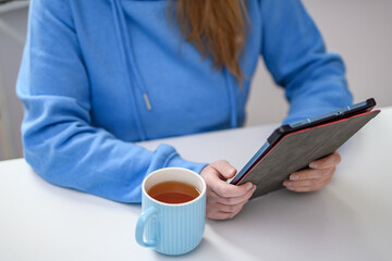 Młoda dziewczyna z kubkiem herbaty w ręce korzysta z tabletu - obrazy, fototapety, plakaty