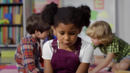 Close-up shot of upset African-American girl crying while playing with another kids in kindergarten