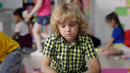 Portrait of sad boy sitting alone in kindergarten playroom