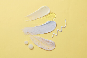 On the light yellow background, four smears of cosmetic texture in yellow, blue and white color are decorated. Gentle skin care