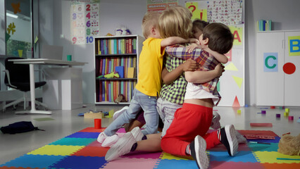 Diverse kindergarten kids hug and have fun in playroom