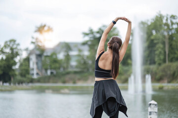 A portrait of a sporty and happy young Asian woman in sportswear is stretching her arms, warming up her body before running outdoors. Outdoor activity concept