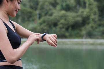 Close-up image of a beautiful and sporty Asian woman in sportswear checking her calories burned and running miles on her smartwatch after a run outdoors.