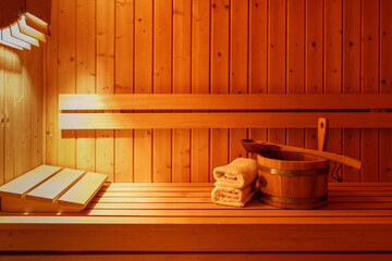 Wooden bucket with spoon, white towels on bench in sauna interior