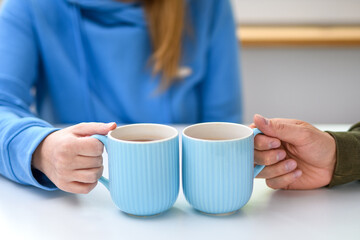 Dwie osoby siedzące przy stole, trzymające w dłoniach kubki z herbatą 