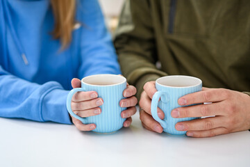 Dwie osoby trzymające w dłoniach kubki z herbatą siedzące przy stoliku w kafejce, z bliska  - obrazy, fototapety, plakaty
