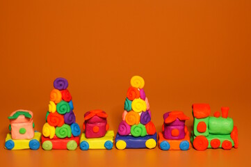 A toy Christmas train made of plasticine with gifts and Christmas trees. Bright orange background. New Year decorations.