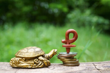 The symbol of the ruble and coins on a green background. There is a turtle figurine next to it....