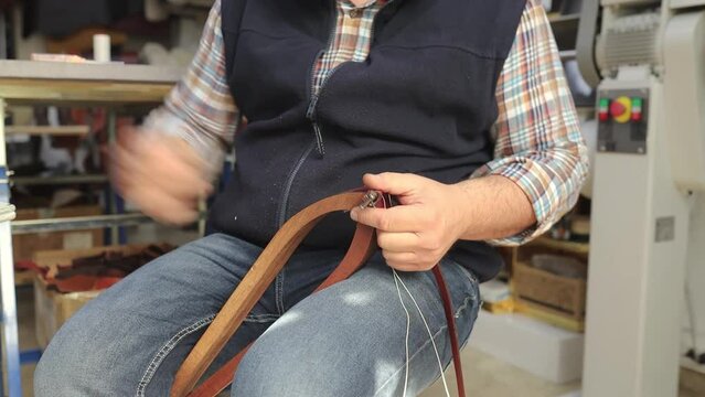 Closeup of leather craftsman hand sewing a belt in workshop