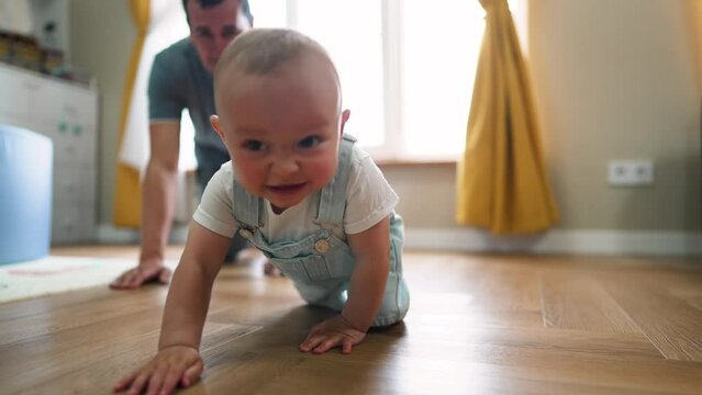 Baby first steps.Toddler at home takes funny first steps.Dad teaches child to walk, legs close-up.Toddler feet on laminate floor.Father's day child education.Kid dream study at home.walk baby learning