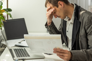 Frustrated overworked caucasian businessman, entrepreneur, product manager, programmer, sits at a desk in the office, massaging the bridge of his nose with his eyes closed, exhausted from long work