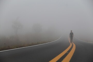 Silhueta de homem nao identificado caminhando na rodovia em amanhecer com neblina 
