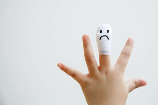 Injured middle finger of child with sad face on bandage