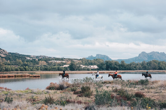 Reiter und Pferde die durch das Meer spazieren in einer spektakul&auml;ren Bergkulisse auf Sardinien in Italien