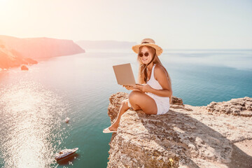 Digital nomad, Business woman working on laptop by the sea. Pretty lady typing on computer by the sea at sunset, makes a business transaction online from a distance. Freelance, remote work on vacation