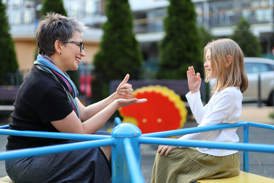 Smiling mature woman talking sign language with a child on the playground.