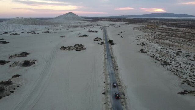 Aerial View Over Dry Arid Landscape Road With Cars Driving Towards Mud Volcano In Background At Hingol National Park . Dolly Forward, Descending Shot
