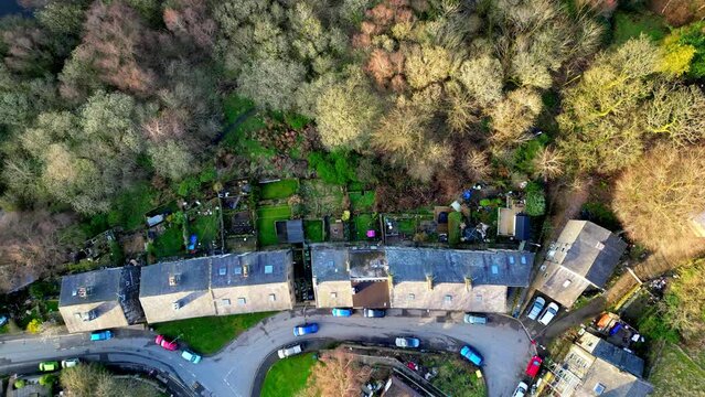 Descending drone shot of green, brown and golden trees and small street in West Yorkshire. As the shot get lower it reveals the tops of houses and gardens in Todmorden