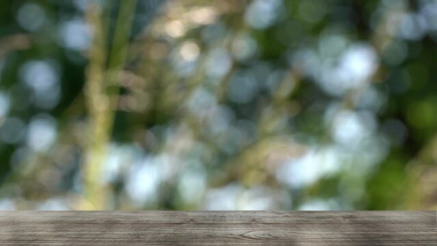 Blurred grasses in slow motion wind and bright defocused lights with empty wooden table in forground for product presentation space, idyllic nature background for vacation, relaxation, pharmacy