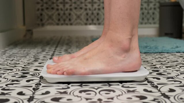 Bare feet woman checking her weight on weighing scales in bathroom. Female measuring her weight using digital scales on floor.