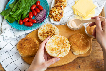 Preparation of all the ingredients for making a burger - bun, cutlet, cheese, salad, tomato, sauces. Top view, girl's hands take a burger roll.