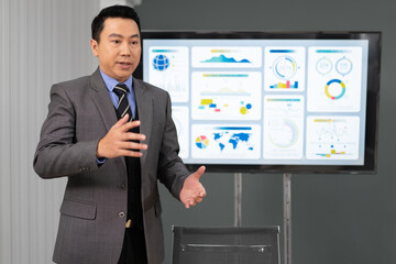 Businessman standing in boardroom giving statistic presentation to committee. Young Asian professional business man talking, presenting strategy planning to executive working team in corporate meeting