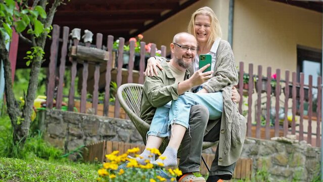 Middle-aged Caucasian couple looking at a smartphone screen while relaxing in the backyard of their country house.