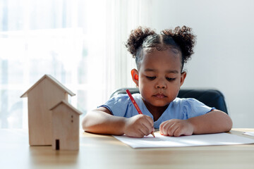 A young African American girl paints with crayons on a white sheet in her living room. preschool...