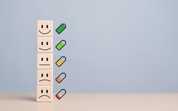 Mentality happiness care. Emotion face symbol on stacked wooden blocks with full to empty battery icons. Life satisfaction level and evaluation, World mental health day. Health and wellness review.