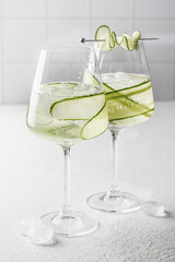 Cucumber infused detox water in glasses with ice. Homemade flavored lemonade on white gray background close up