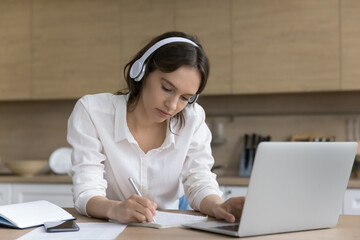 Serious young woman writes test, listen audio class take part in on-line study, gain new knowledge...