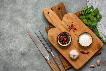 Culinary background. Wooden cutting boards, spices, greens and kitchen tools on a gray concrete background. Top view, flat lay.