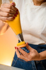 Woman with confectionery bag in hands squeezing tasty cream filling to fresh macarons shells
