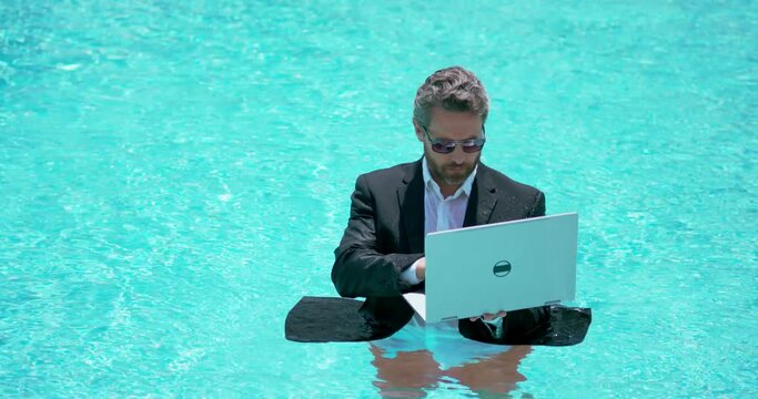 Business man in suit working on laptop in swimming pool. Travel tourism and business concept. Crazy male Business office employee using laptop in pool on summer day. Summer Business.